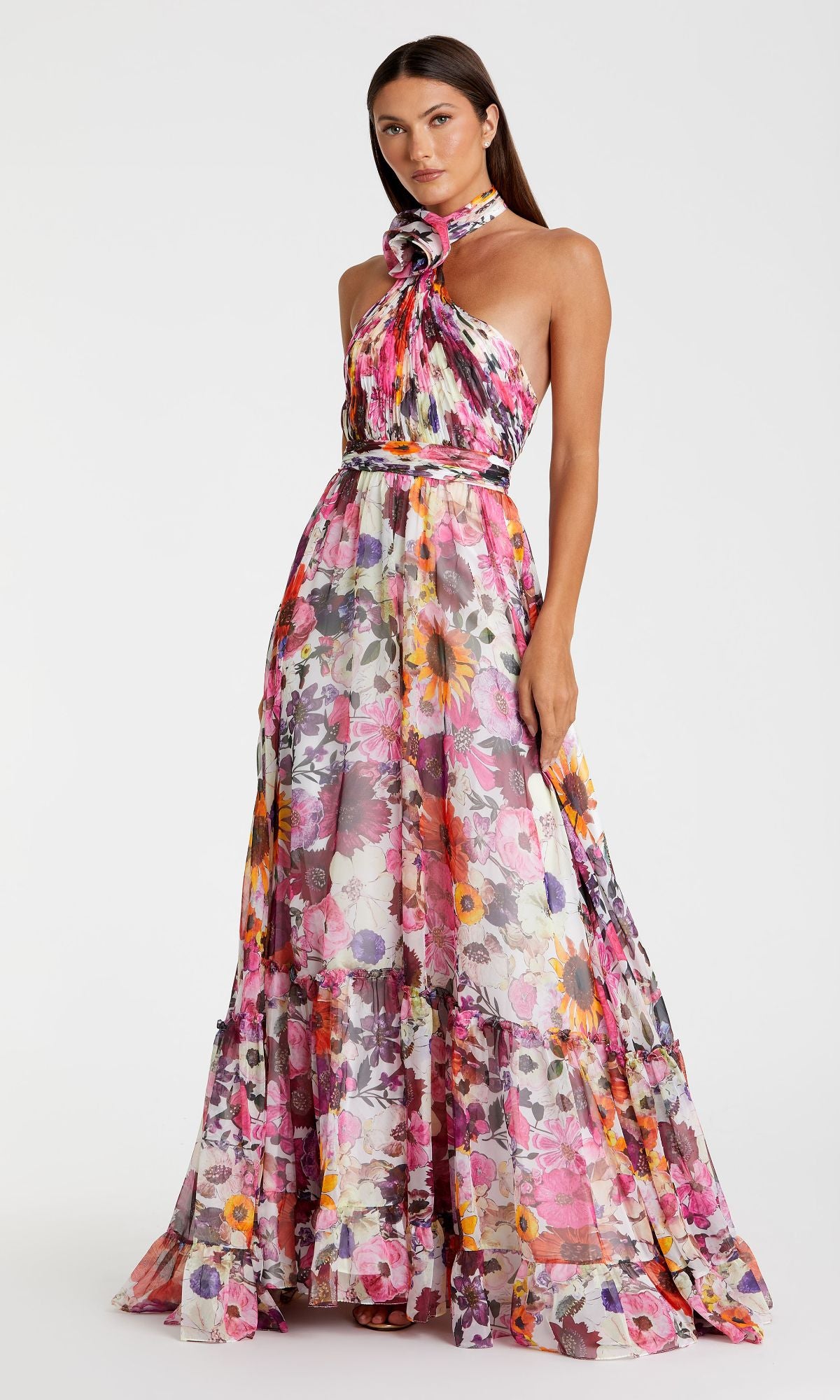 A woman stands wearing a Mac Duggal 68101 Long Print Halter Formal Dress, featuring a floor-length design, sleeveless cut, floral print, halter neckline, and a full flowing skirt.